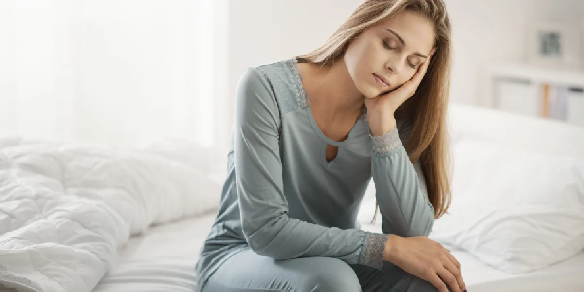 Woman sitting on bed looking fatigued, symbolizing symptoms of PCOS in South Ogden, UT.