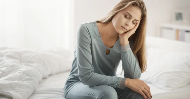 Woman sitting on bed looking fatigued, symbolizing symptoms of PCOS in South Ogden, UT.