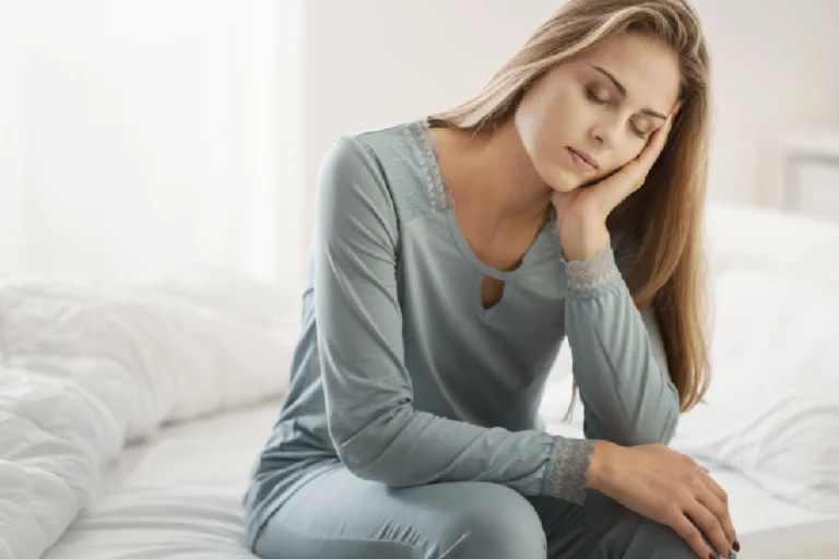 Woman sitting on bed looking fatigued, symbolizing symptoms of PCOS in South Ogden, UT.