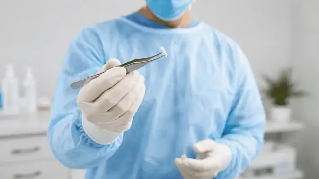 hormone-pellet-therapy-medical-provider-holding-pellet Healthcare provider in a clinical setting holding a hormone pellet with sterile tweezers before a hormone pellet therapy procedure.